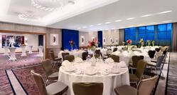 Varadinum Ballroom With With Place Settings, Flowers and White Linens on Round Tables, Chairs, Windows With Sheer Drapes, and View of Cocktail Tables and Wall Art in Breakout Room