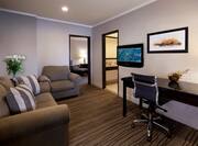 TV, Wall Art, Work Desk, Sofa, Armchair, And Open Doorways to Bedrrom and Bathroom in Living Room of Junior Suite  