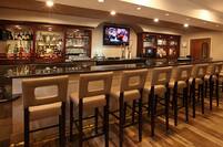 Angled View of Counter Seating and TV at Fully Stocked Bar