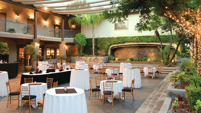 Candles and White Linens on Dining and Cocktail Tables, Chairs, Bar and Food Service Tables Set Up in Courtyard for an Event