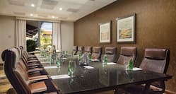 Wall Art, Window With Open Drapes, and Seating for 14 at Boardroom Table With Drinking Glasses and Bottled Water