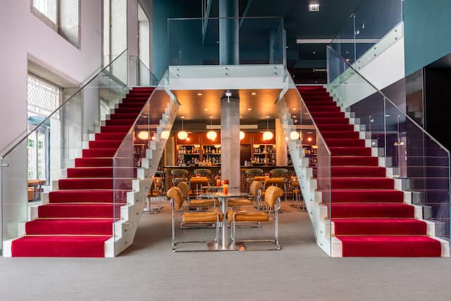 Espace hall avec grand escalier double avec tapis rouges, tables et chaises