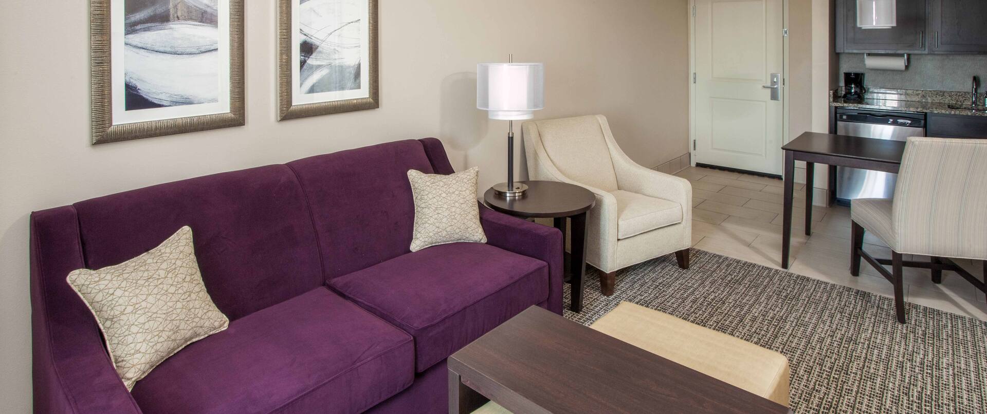 Two Room Suite Living With Purple Sofa, Wall Art, Arm Chair, Dining Table, Kitchen and View of Entry
