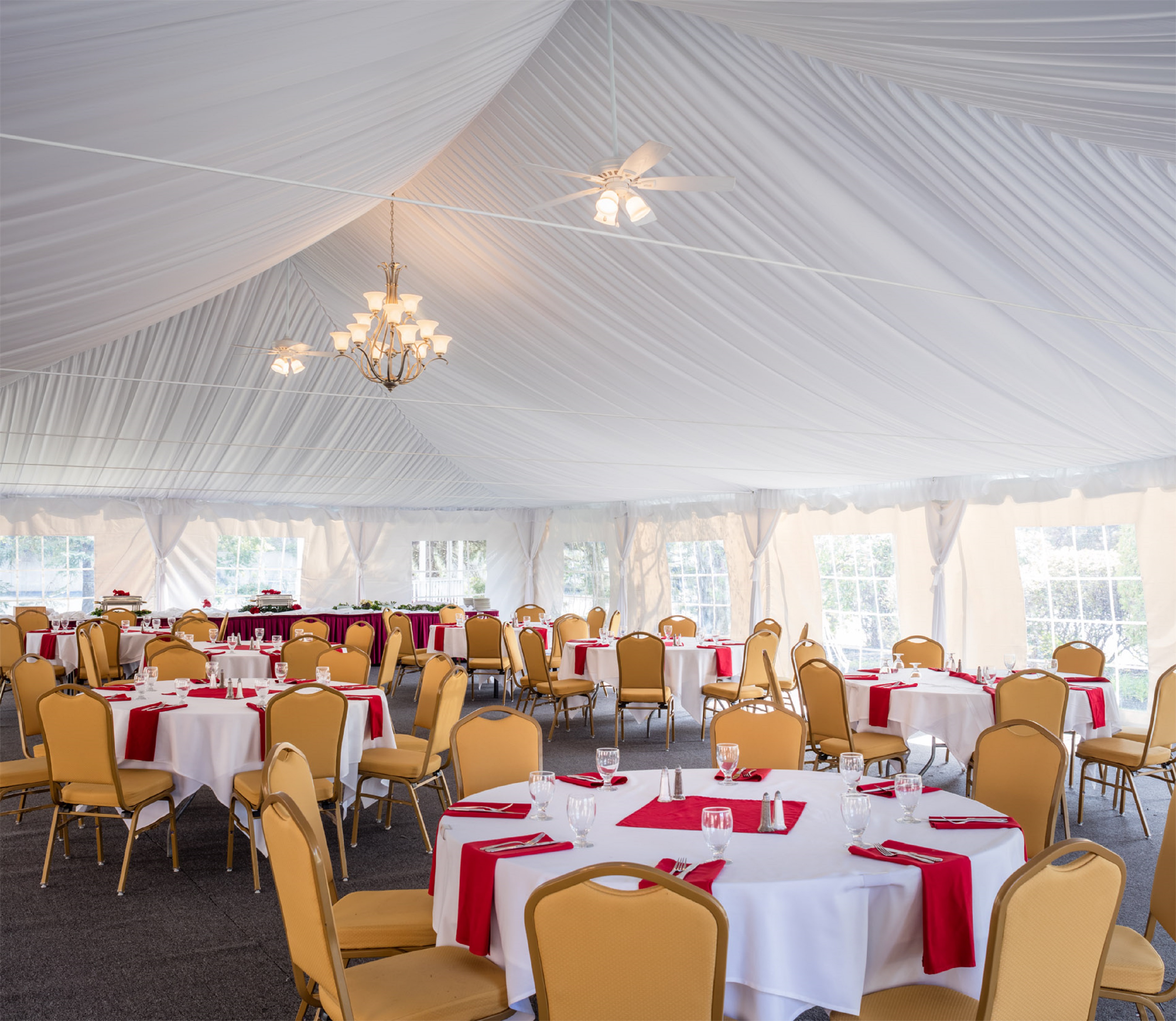 Drinking Glasses, Silverware, Red Napkins, and White Linens on Banquet Tables and Food Service Area Set Up for Event Under White Pavilion Tent