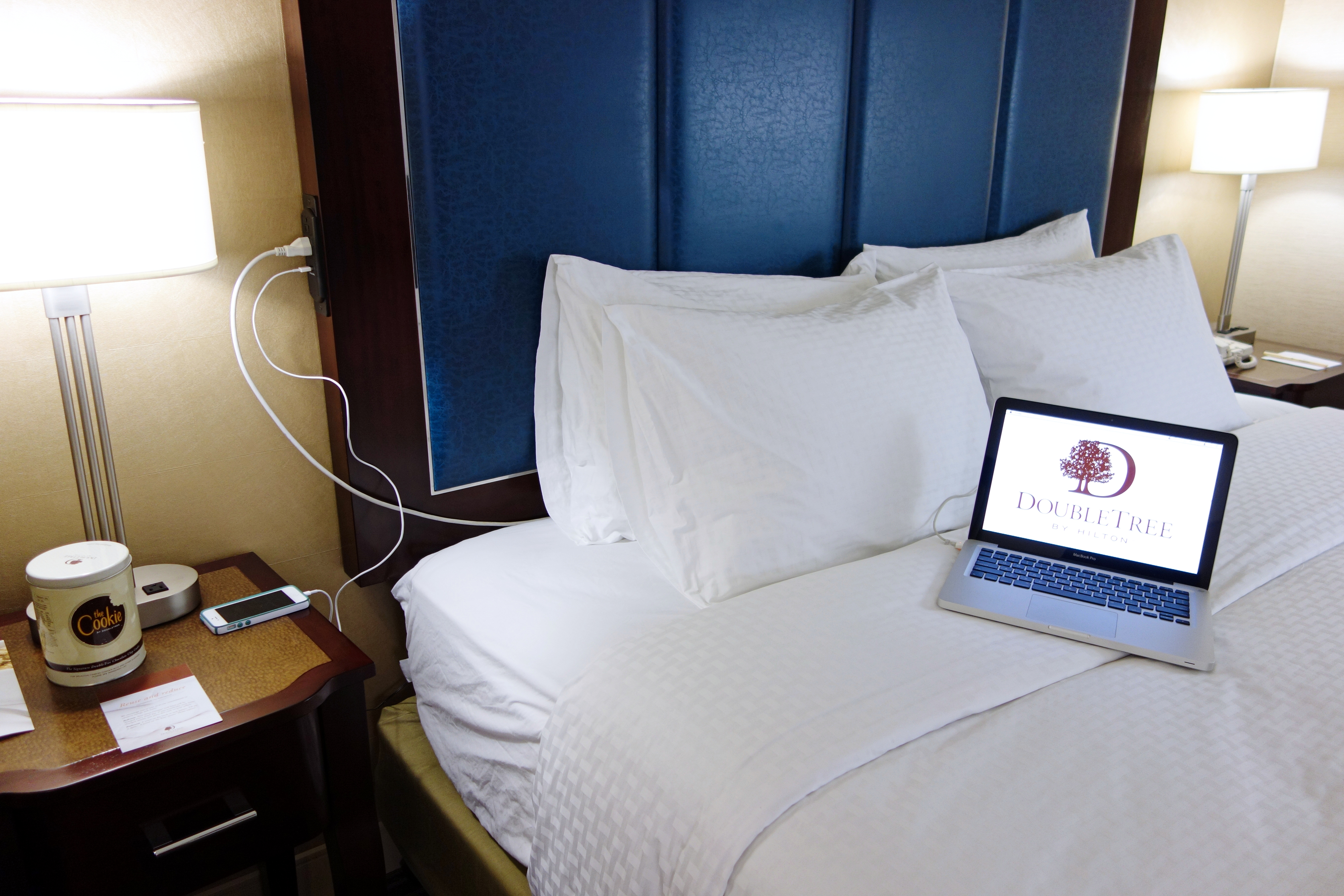 King Bed With Laptop and Phone Plugged Into Connectivity Headboard, and Bedside Tables With Illuminated Lamps