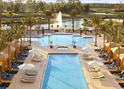 View of Two Pools Flanked by Palm Trees, Cabanas, and Loungers with Fountain in Background