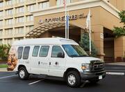 Daytime View of Hotel Shuttle With Cookie Graphic Parked in Front of Hotel Exterior, Flagpoles, and Landscaping
