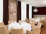 Paris Restaurant Dining Area With Place Settings, Flowers, and White Linens on Tables, Beige Chairs, Windows With Long Drapes, Wall Art, and Decorative Lighting