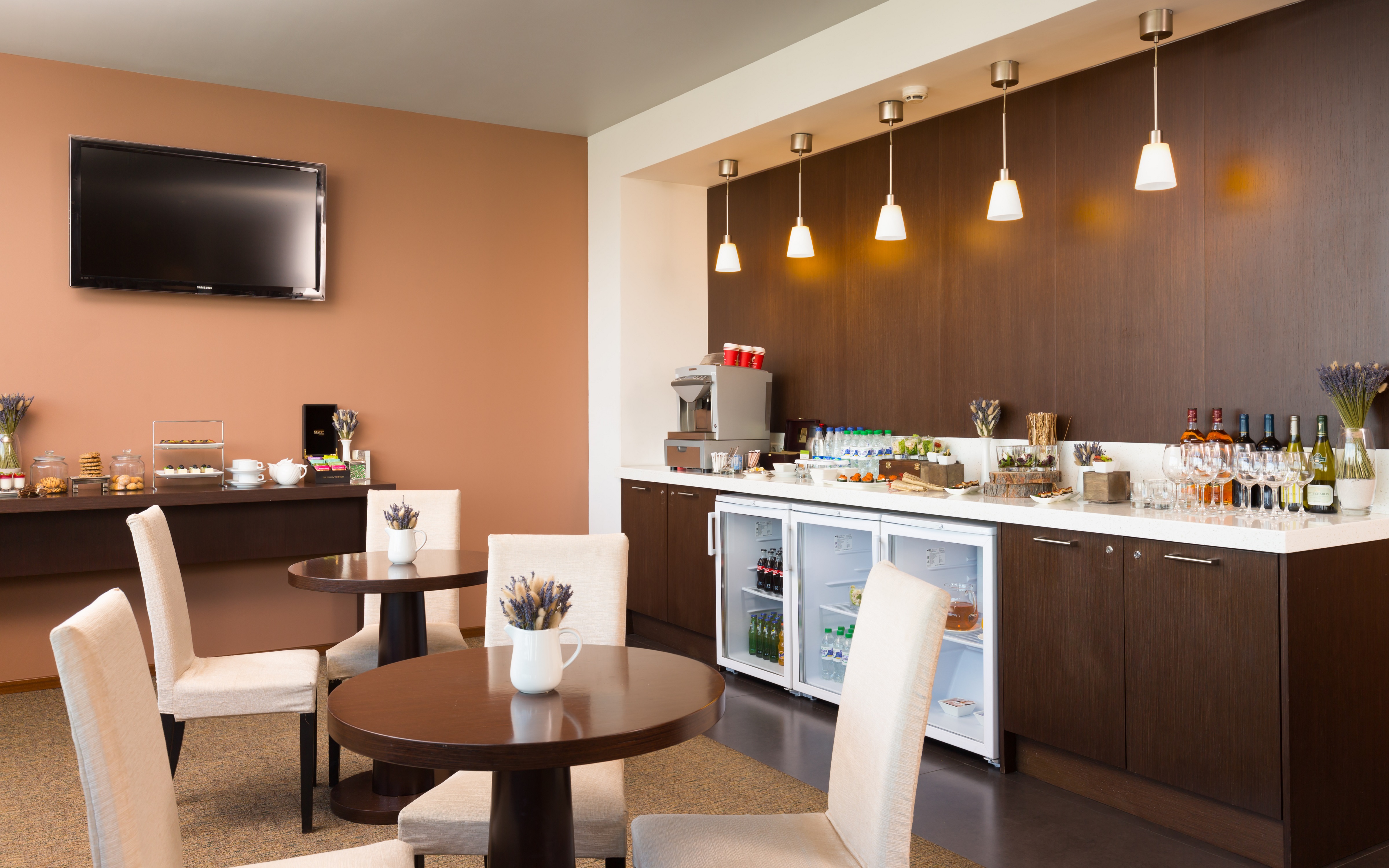 Two Round Tables With White Chairs, TV, and Refreshments on Counters in Executive Lounge  