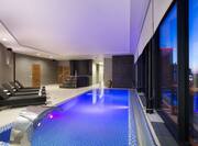 Illuminated Indoor Pool With Lounge Seating and Windows With Night View