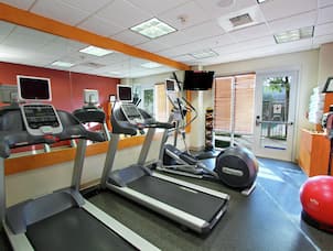 Fitness Center With Cardio Equipment Facing Mirrored Wall, TV, Weight Balls, Glass Entry Door, Towel Station, and Red Stability Ball