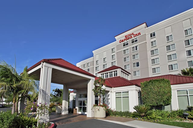 Daytime View of Hotel Exterior With Signage, Landscaping, and Porte Cochère