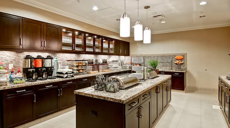 Breakfast serving area with buffet trays, coffee, juice, pastries, fruits, and dining amenities