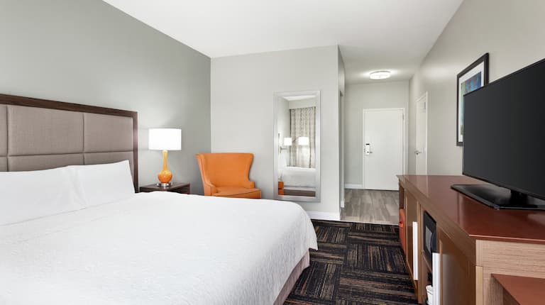 Spacious accessible guest room featuring comfortable king bed, TV, and lounge chair.