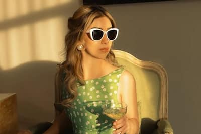 Girl wearing a green polka dot dress with white sunglasses on holding a cocktail in the sun.
