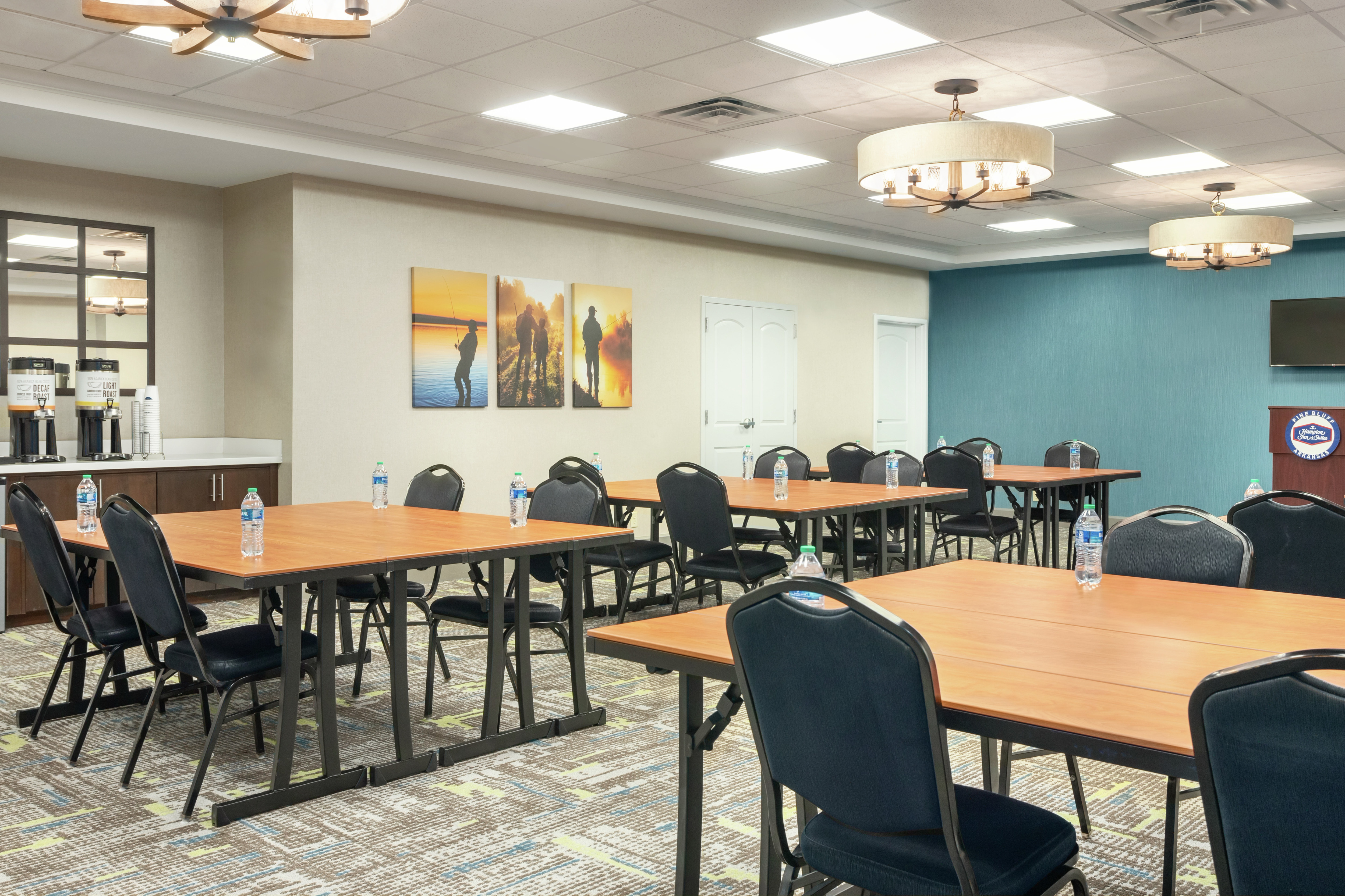 Spacious meeting space featuring large tables with ample seating for events, TV, podium, and coffee break station.