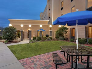 Spacious outdoor patio area featuring lush landscaping, glowing guest room windows, and beautiful dusk sky.