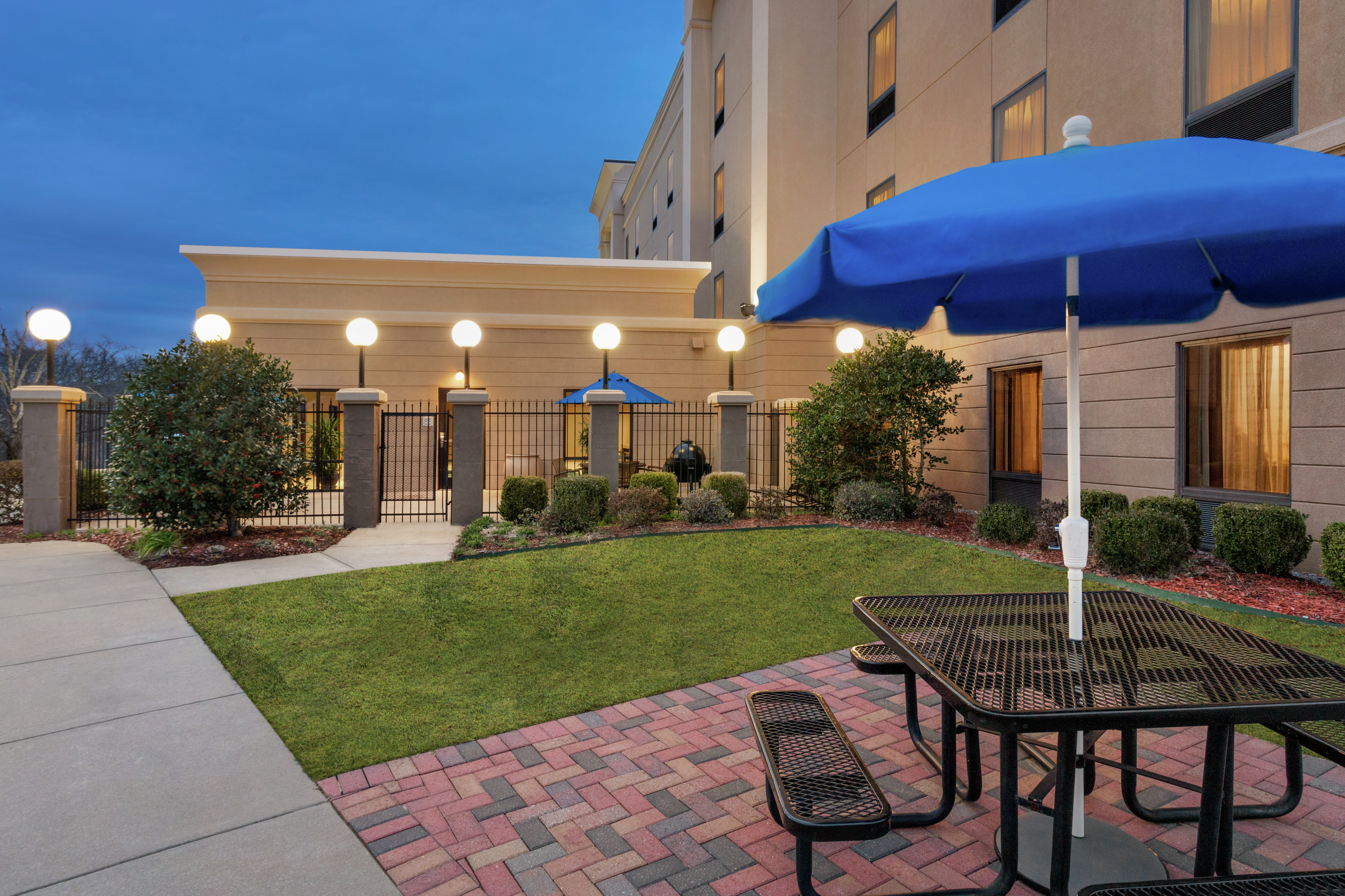 Spacious outdoor patio area featuring lush landscaping, glowing guest room windows, and beautiful dusk sky.