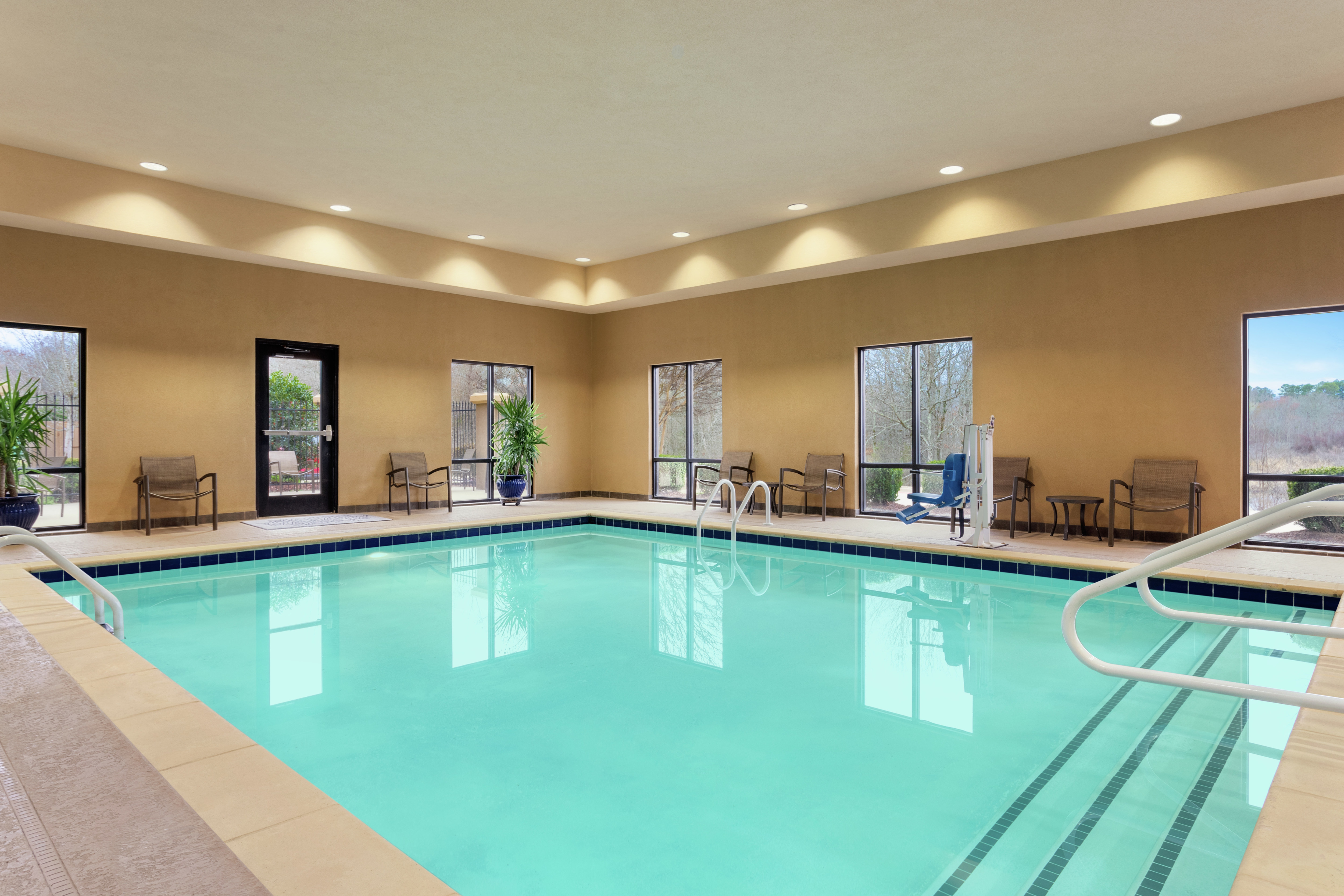 Spacious indoor pool featuring large windows with ample natural light, access to outdoor patio, and accessible chair-lift.