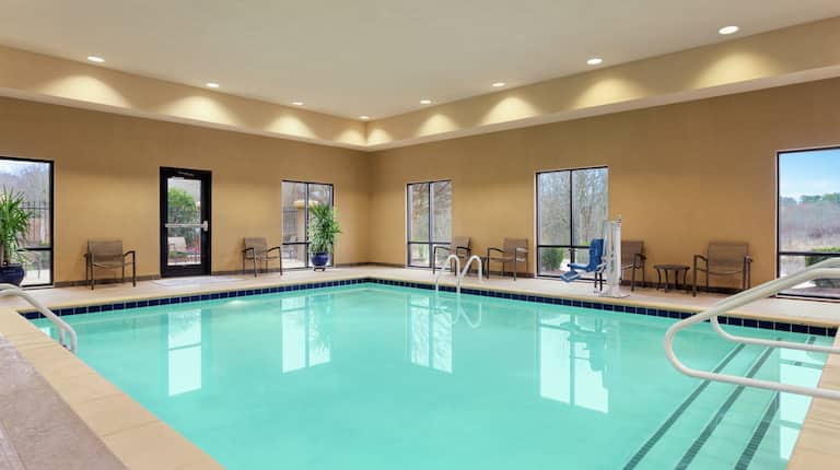 Spacious indoor pool featuring large windows with ample natural light, access to outdoor patio, and accessible chair-lift.