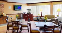 Yellow Flowers on Tables, Chairs, Soft Seating, Illuminated Floor Lamps, TV, Food Service Area and Windows With Sheer Drapes