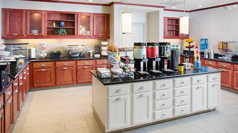 Breakfast serving area with buffet trays, coffee, juice, snacks, fruits, and dining amenities