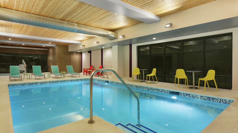 Large indoor pool featuring floor to ceiling windows, lounge chairs, accessible chair lift, and hot tub.