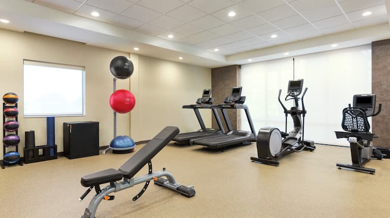 Spacious fitness center featuring cardio machines, workout bench, and medicine balls.