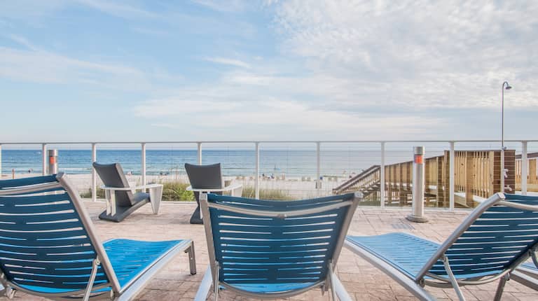 Beach View From Hotel Patio With Blue Loungers and Chairs