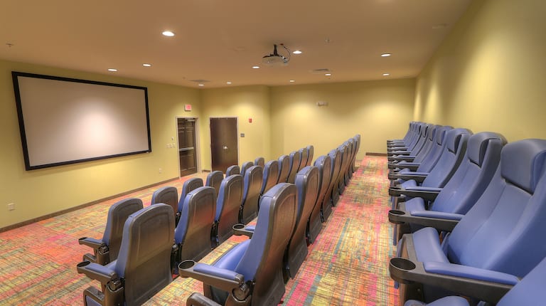 On-Site Theater With Four Rows of Blue Chairs Facing Projector Screen, Overhead Projector, and Entry Door