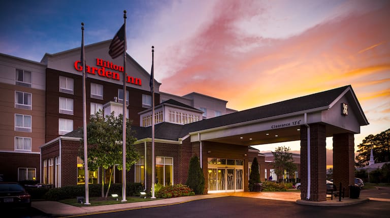 Hotel Exterior With Signage, Flagpoles, Landscaping, and Porte Cochère at Sunset