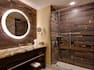 Brightly Lit Round Vanity Mirror, Sink, Towels, Toiletries, Amenities, and Shower With Glass Doors in Suite Bathroom