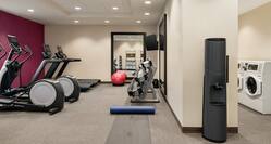 Spacious fitness center featuring cardio machines, free weights, yoga mats, and conveniently located next to guest laundry.