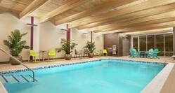 Indoor swimming pool featuring beautiful wood ceiling, patio furniture, lush plants, and floor to ceiling windows.