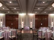 Place Settings, White Napkins, and Drinking Glasses on Dining Tables With Pink Linens and Dance Floor Set Up in Meeting Space For Banquet