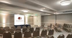 Meeting Room Arranged Theater Style With White Entry Door, Rows of Chairs Facing Projector Table and Presentation Screen