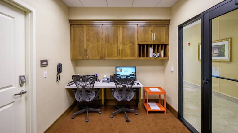 Business Center With Computer Workstation, Too Ergonomic Chairs, Overhead Cabinets, and Glass Entry Door