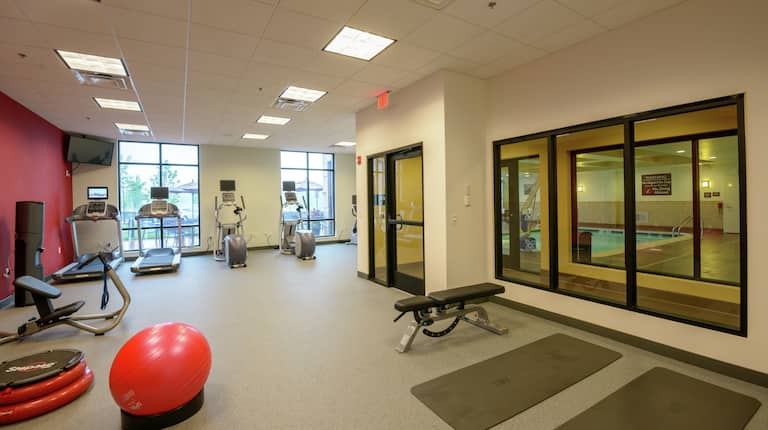 Fitness Center With TV, Cardio Equipment, Weight Bench, View Into Indoor Pool, Red Stability Ball, Aerobic Stepper, and Water Cooler
