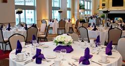Fireplace in Meeting Room With Flowers, Place Settings, and White Linens on Round Tables Set Up For Daytime Banquet