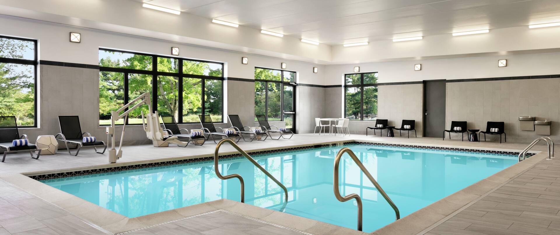 Indoor swimming pool featuring large windows with beautiful outside view, lounge chairs, and accessible chair lift.