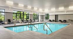 Indoor swimming pool featuring large windows with beautiful outside view, lounge chairs, and accessible chair lift.