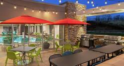 Outdoor patio featuring ample seating with umbrellas, string lights, and BBQ grills.