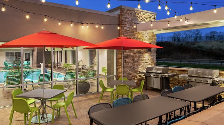 Outdoor patio featuring ample seating with umbrellas, string lights, and BBQ grills.