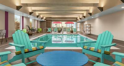 Bright indoor pool featuring chairs around table, large windows, and pool in background.