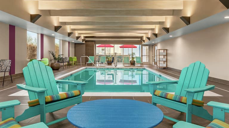 Bright indoor pool featuring chairs around table, large windows, and pool in background.