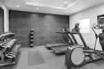 Bright fitness center featuring cardio machines, yoga mat, free weights, and TV.