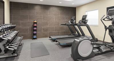 Bright fitness center featuring cardio machines, yoga mat, free weights, and TV.