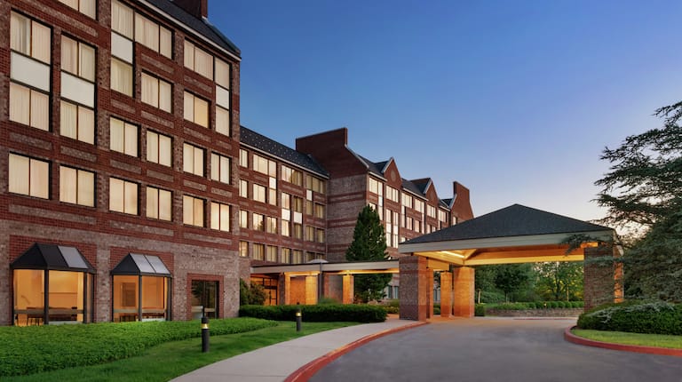Welcoming Embassy Suites hotel featuring porte cochere, glowing guestroom windows, and beautiful dusk sky.