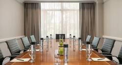 Bright meeting room featuring large boardroom table, notepads and pens, and complimentary beverage.
