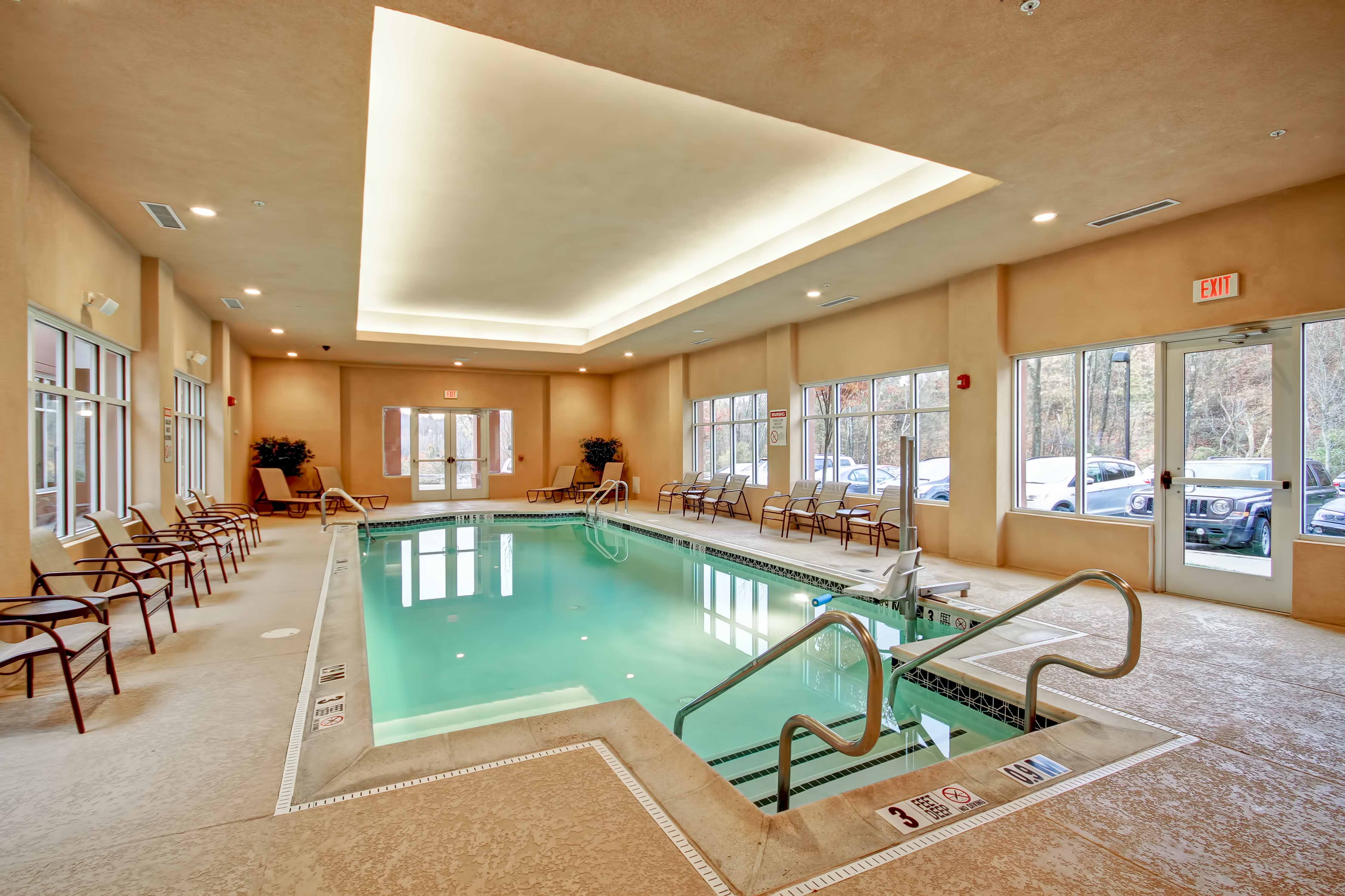 Indoor pool with lounge chairs and outdoor view through windows